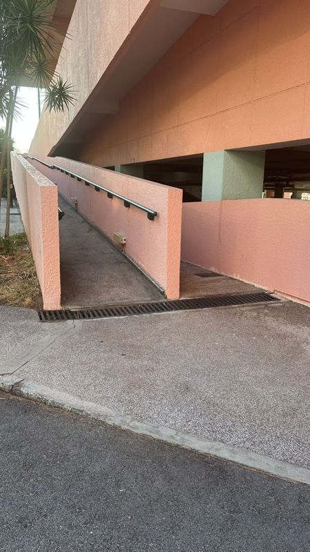 Paved wheelchair path leading towards the entrance of an outdoor swimming pool